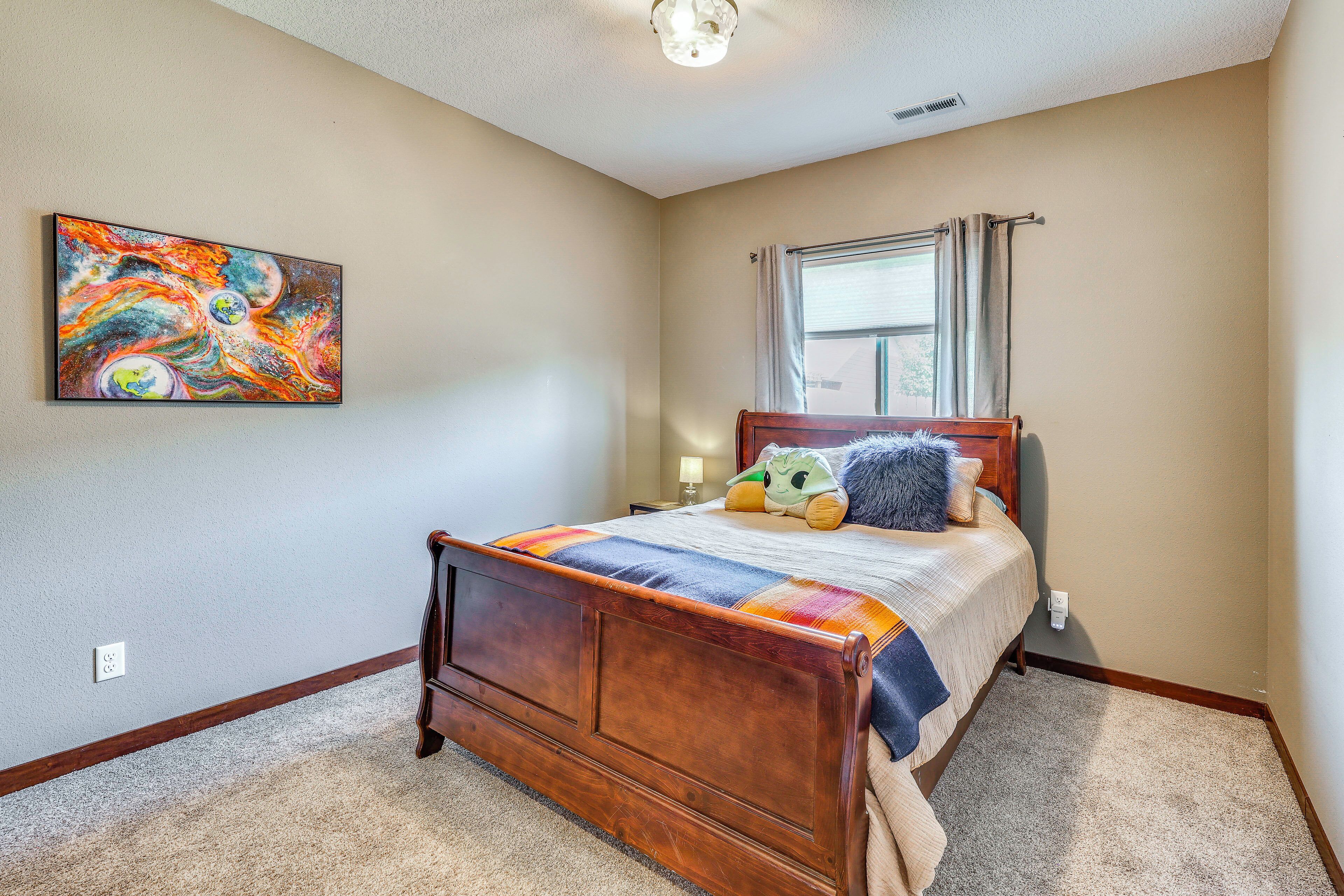 A bedroom with a wooden bed, a colorful abstract painting, and a window with curtains.