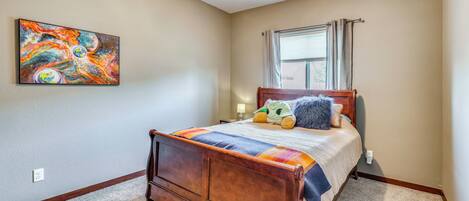 A bedroom with a wooden bed, a colorful abstract painting, and a window with curtains.