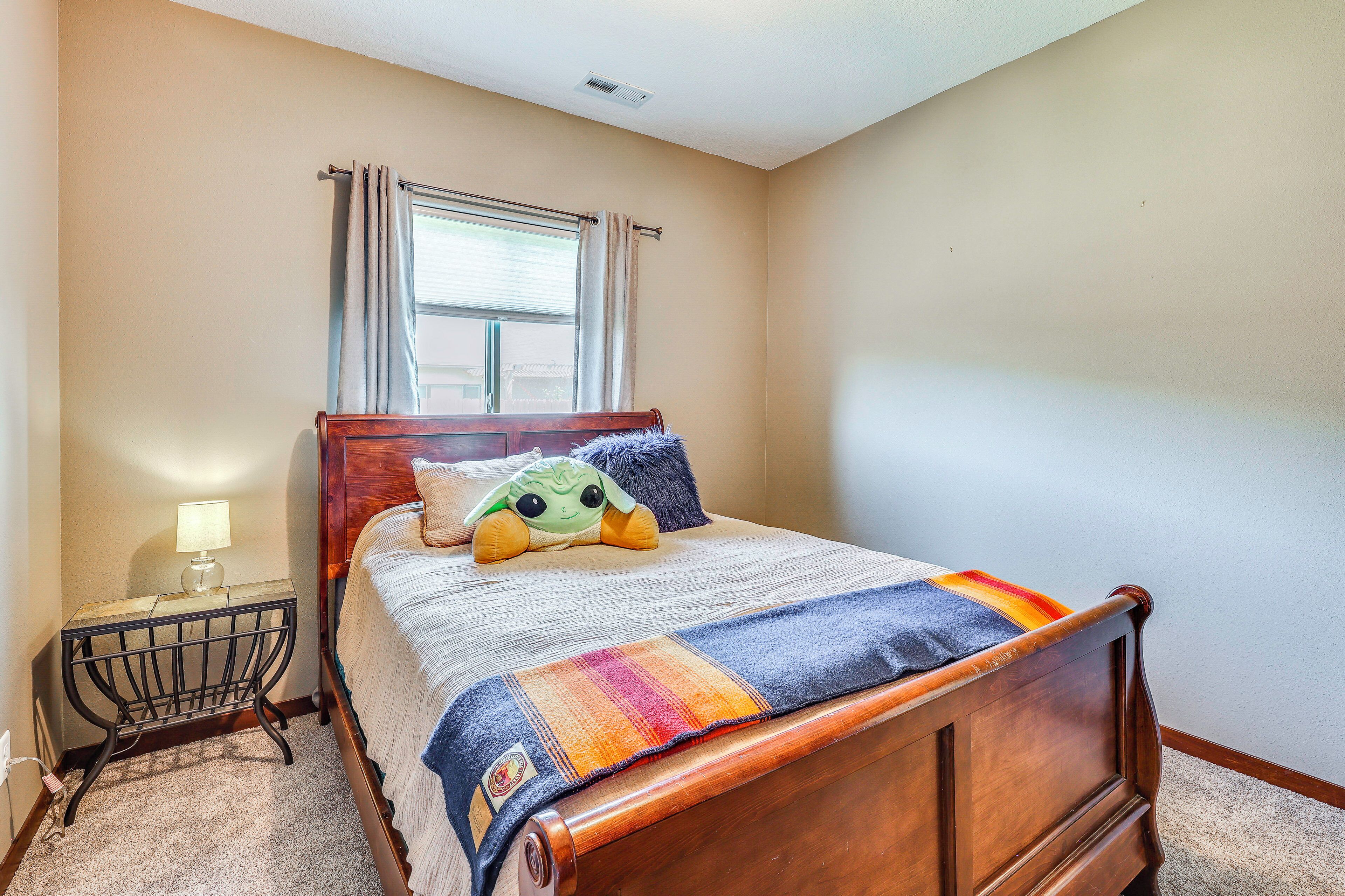 A bedroom with a wooden bed, a nightstand with a lamp, a window with curtains, and a plush toy on the bed.