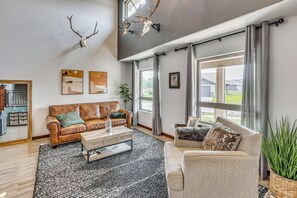 A spacious living room with a leather sofa, a coffee table, and a large window with curtains. - Private Yard w/ Patio! Rapid City Escape (Rapid City)