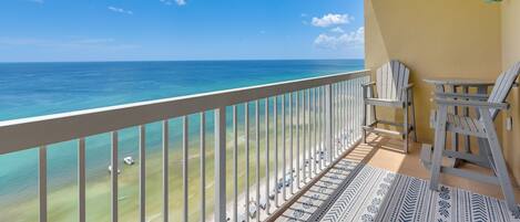 A balcony with a view of the ocean, a chair, and a patterned rug.