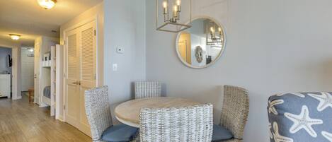 A dining area with wicker chairs, a round table, and a mirror on the wall.