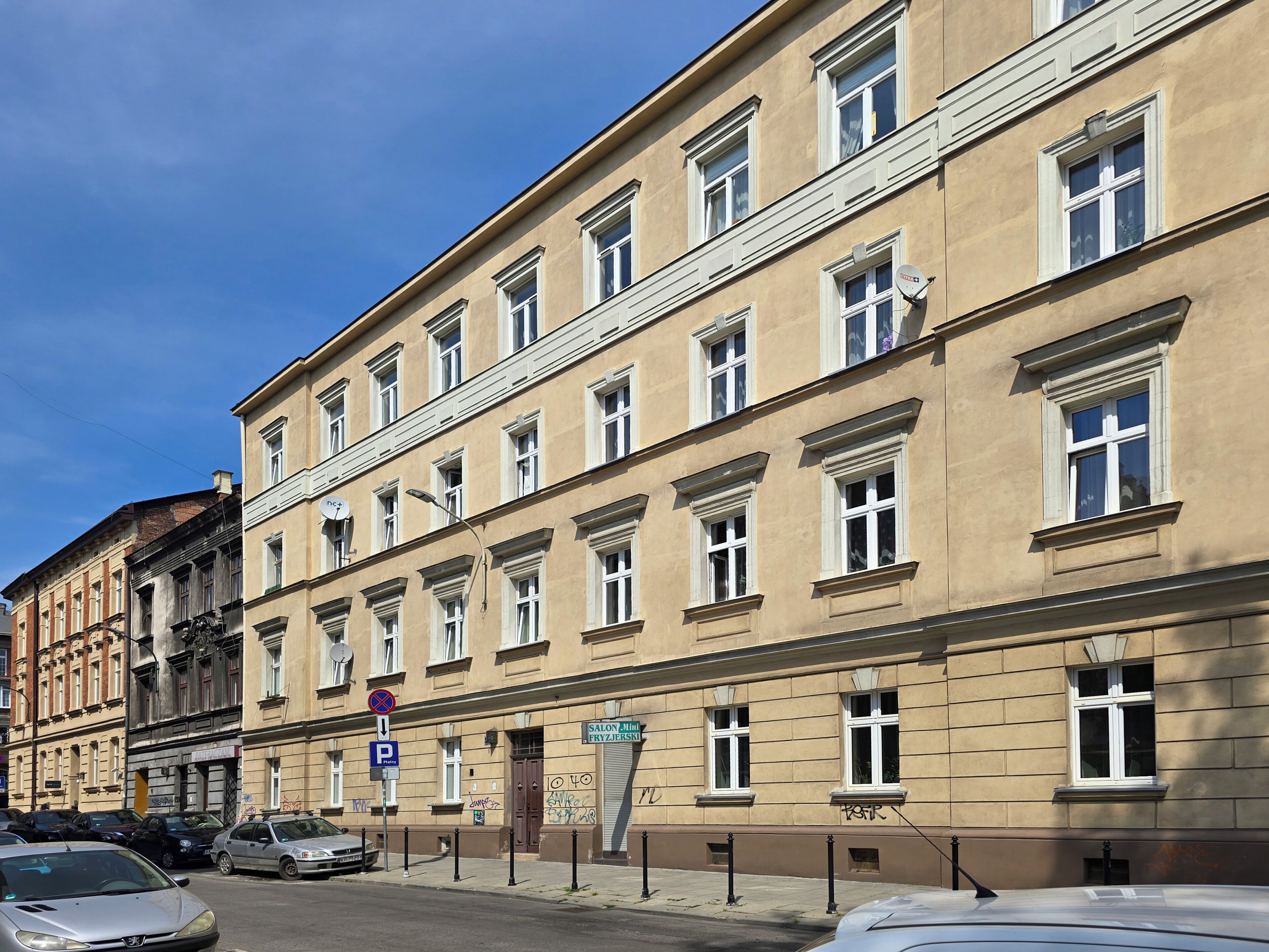 Un edificio a più piani con una fila di finestre, un ingresso ben visibile e una strada con auto parcheggiate.