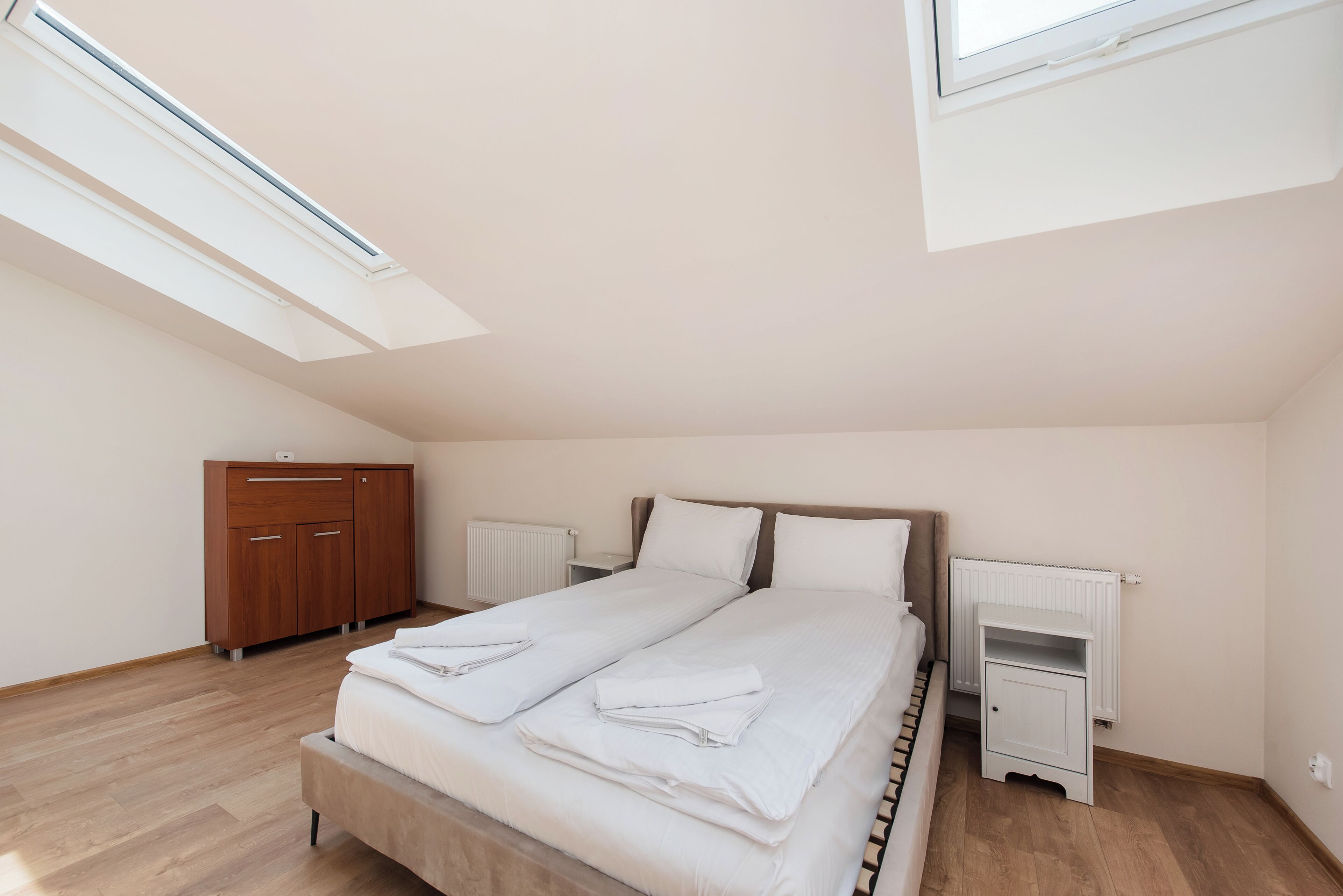A bedroom with a bed, a wardrobe, a radiator, and skylights.