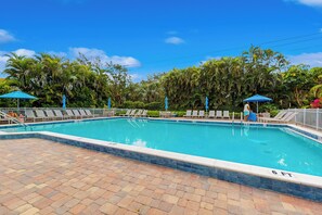 A rectangular swimming pool with a tiled edge, surrounded by lounge chairs and umbrellas, set against a backdrop of lush greenery and palm trees. - < 1 Mi to Beach! Top-floor Naples Retreat w/ Pool (Naples)