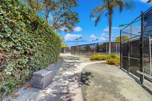 A pathway flanked by a tall hedge and a chain-link fence, leading to a building with a clear blue sky above. - < 1 Mi to Beach! Top-floor Naples Retreat w/ Pool (Naples)
