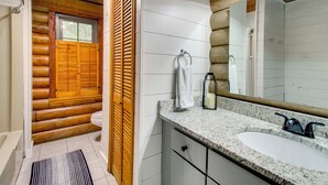 A bathroom with a wooden log wall, a white sink, and a mirror. - Pool & Fishing at Lakefront Midway Retreat (Midway)