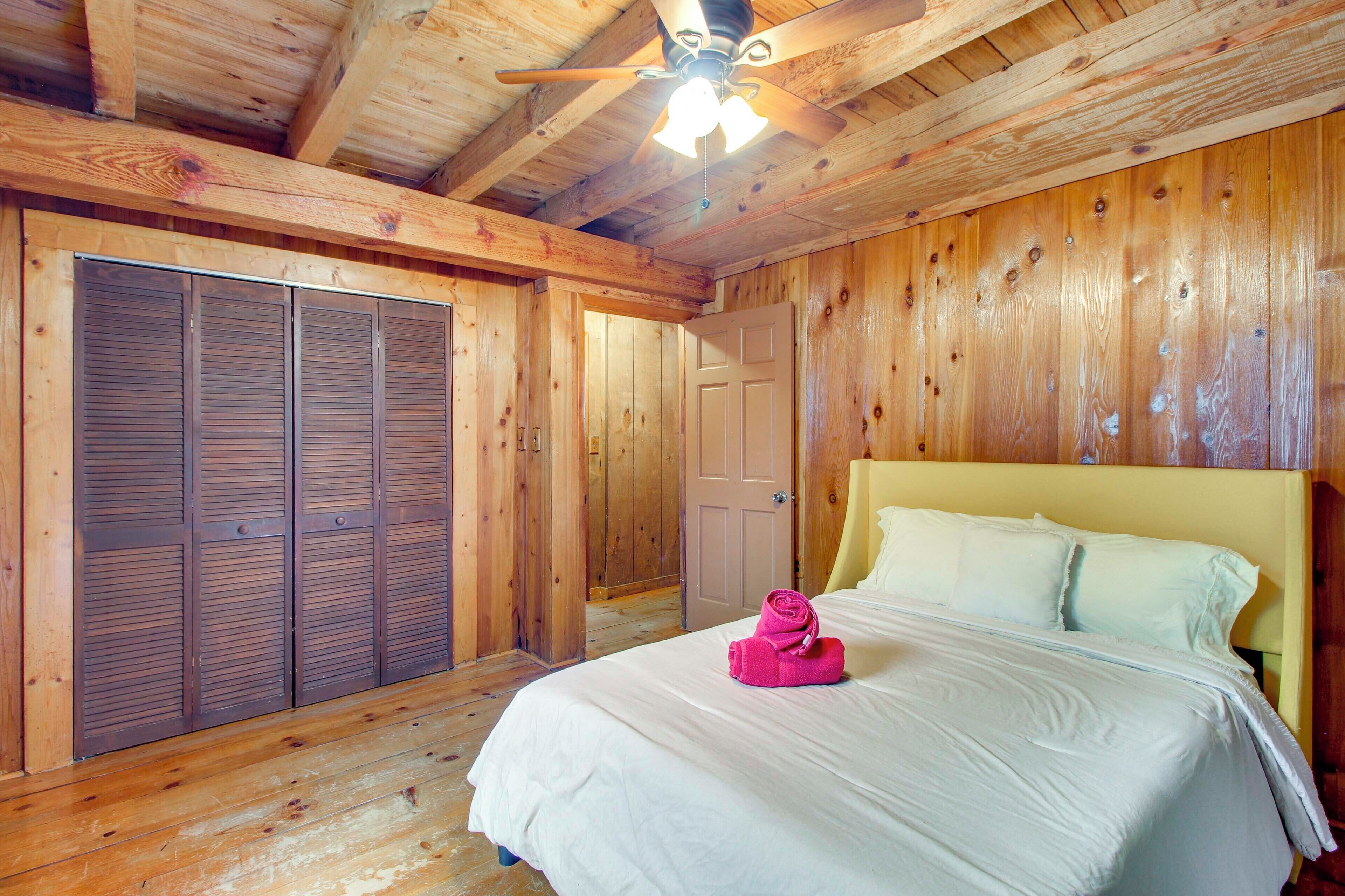 Een kamer met houten vloer, een bed, een plafondventilator en een deur.