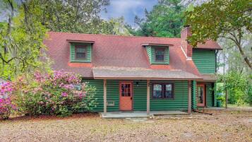 A two-story log cabin with a green exterior, a red roof, and a front porch.