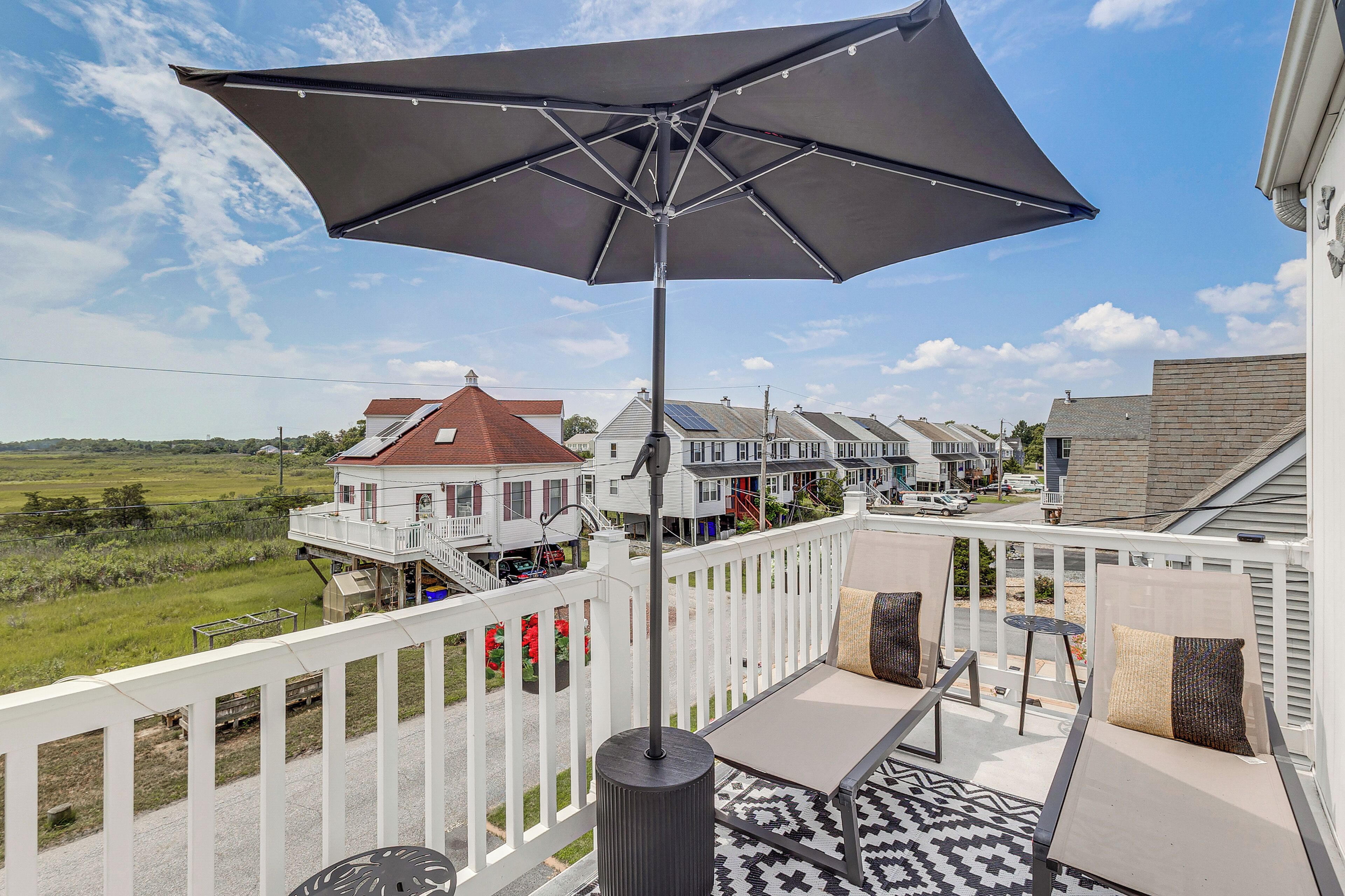 A balcony with a large umbrella, outdoor seating, and a view of a row of houses.