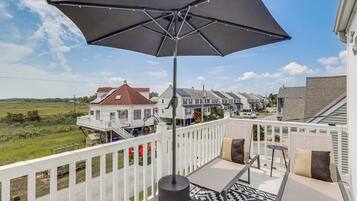 A balcony with a large umbrella, outdoor seating, and a view of a row of houses.