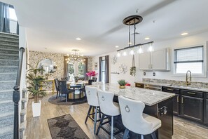 A modern kitchen with a marble countertop, stainless steel appliances, and a dining area with a patterned wall and a chandelier.
