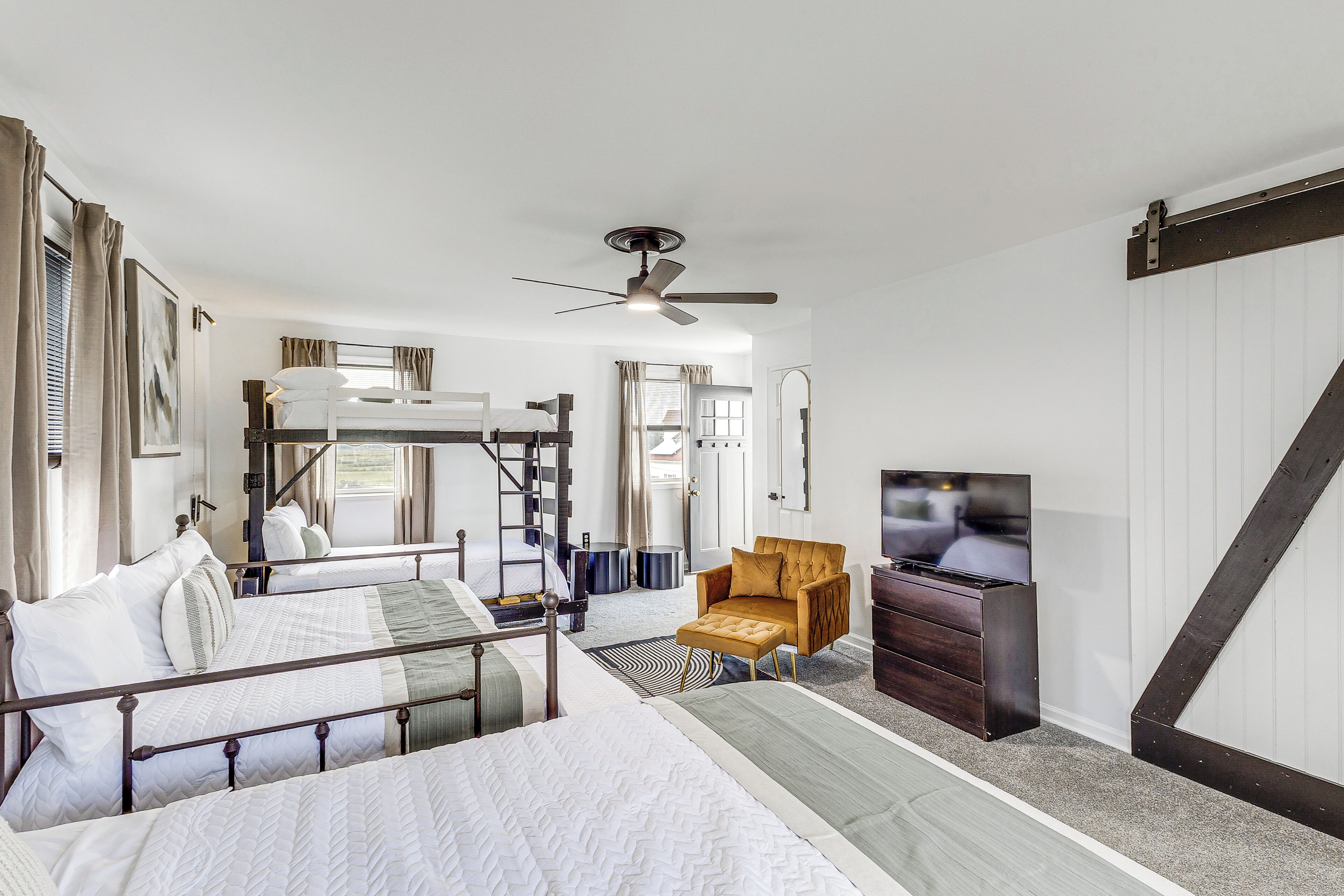 A room with bunk beds, a ceiling fan, a television, and a wooden chair.