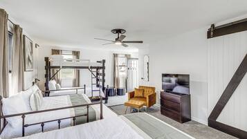 A room with bunk beds, a ceiling fan, a television, and a wooden chair.
