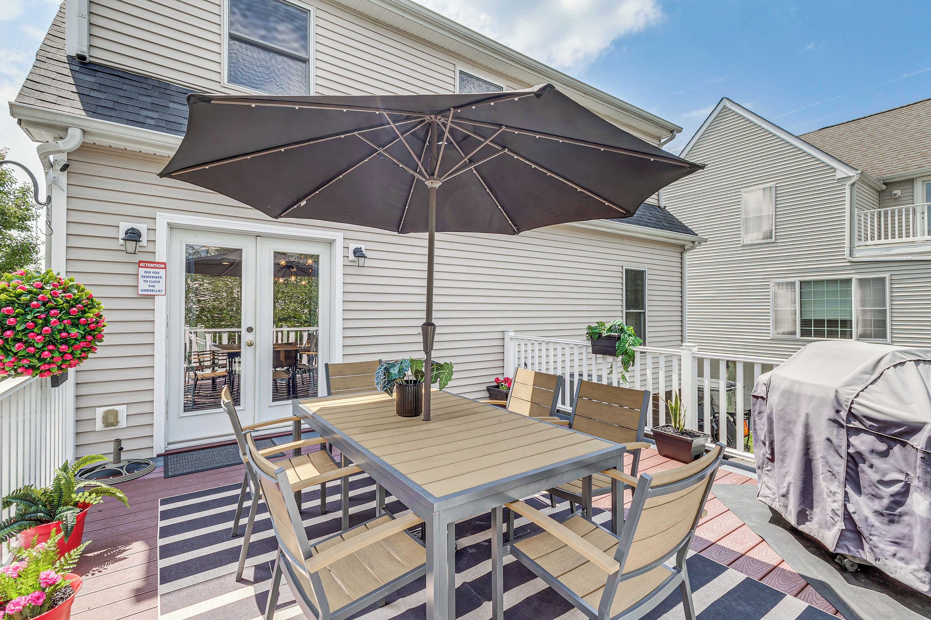 En terrasse med et bord, stole, en parasol og en grill med tag.