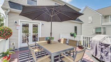 En terrasse med et bord, stole, en parasol og en grill med tag.