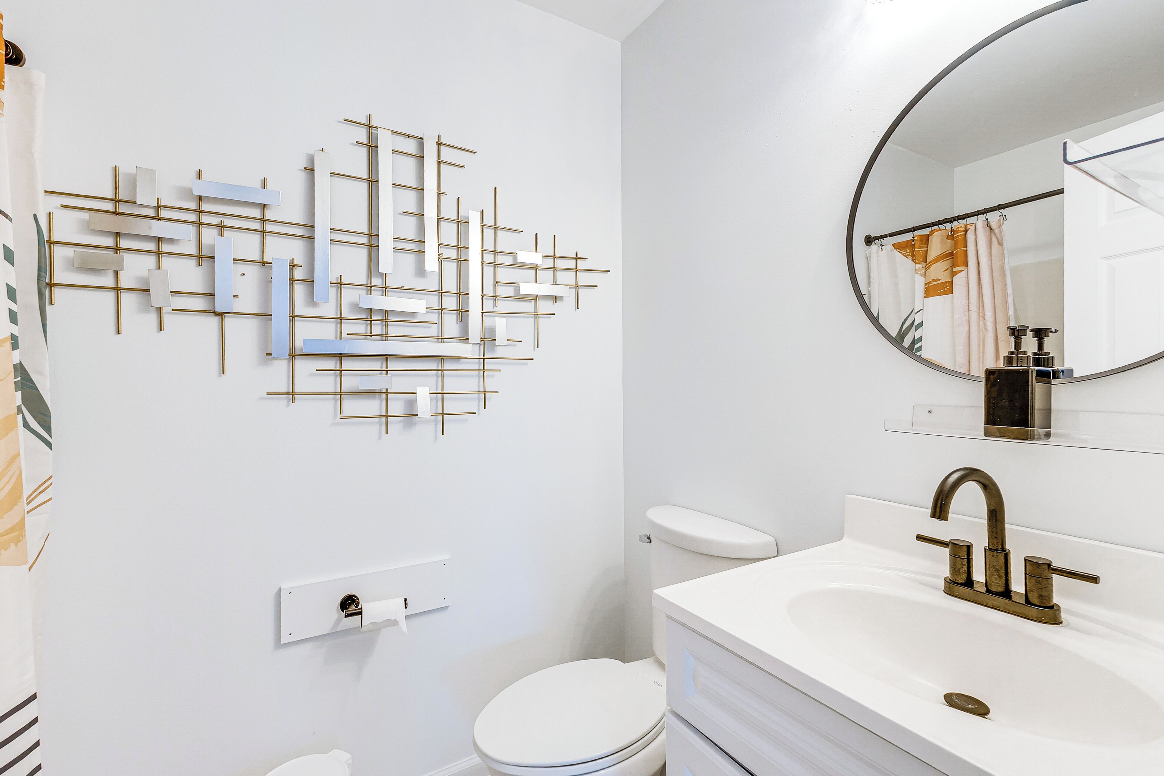 A bathroom with a modern design, featuring a toilet, a sink with a gold faucet, and a wall-mounted towel rack.