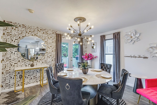 A dining area with a round table, chairs, a chandelier, and patterned wallpaper.