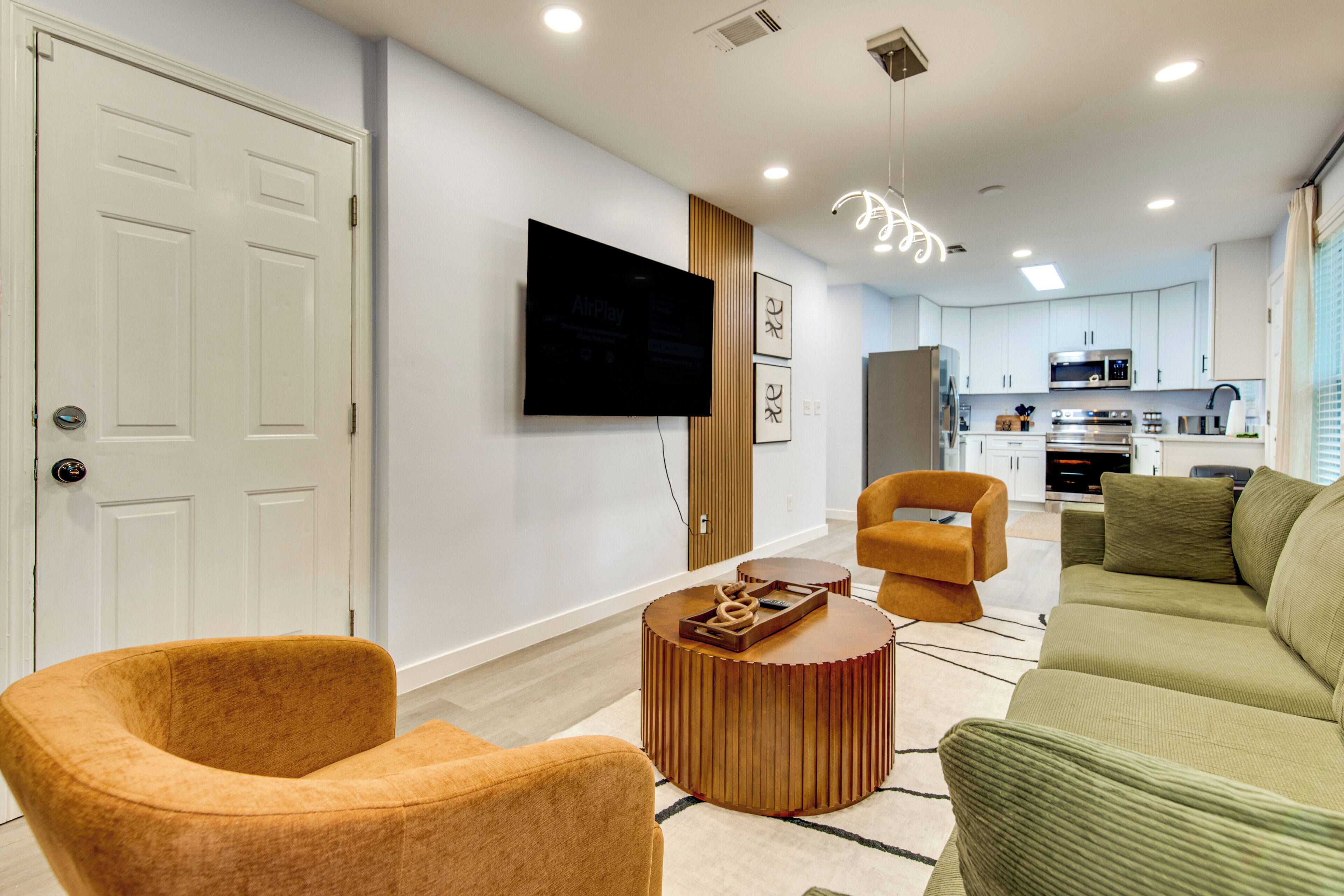 A modern living room with a flat-screen TV, two sofas, a coffee table, and a kitchen in the background.