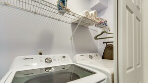 Ett tvättrum med en tvättmaskin och en torktumlare från Samsung, båda med frontmatning, samt en torkställning och en handduksställning.