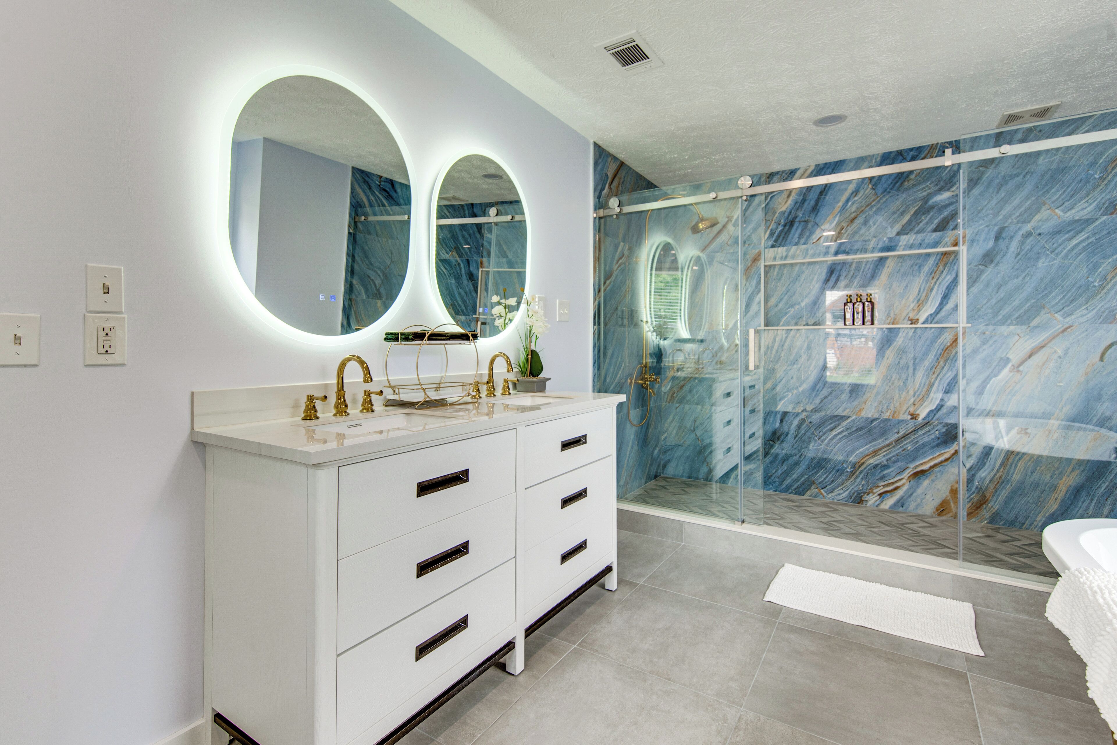 Un baño moderno con un tocador blanco, dos espejos grandes y una cabina de ducha de vidrio con azulejos de mármol.