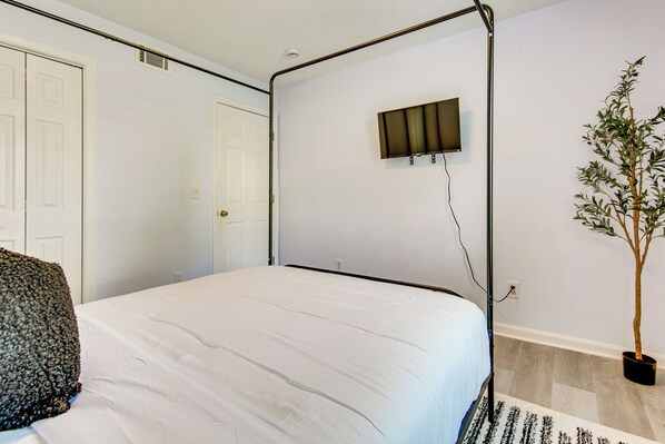 A bedroom with a four-poster bed, a television mounted on the wall, and a potted plant.