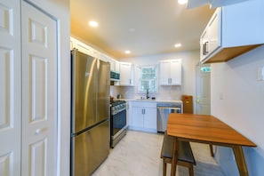 Una cocina compacta con gabinetes blancos, un refrigerador de acero inoxidable, un horno empotrado y una mesa de madera con un banco.