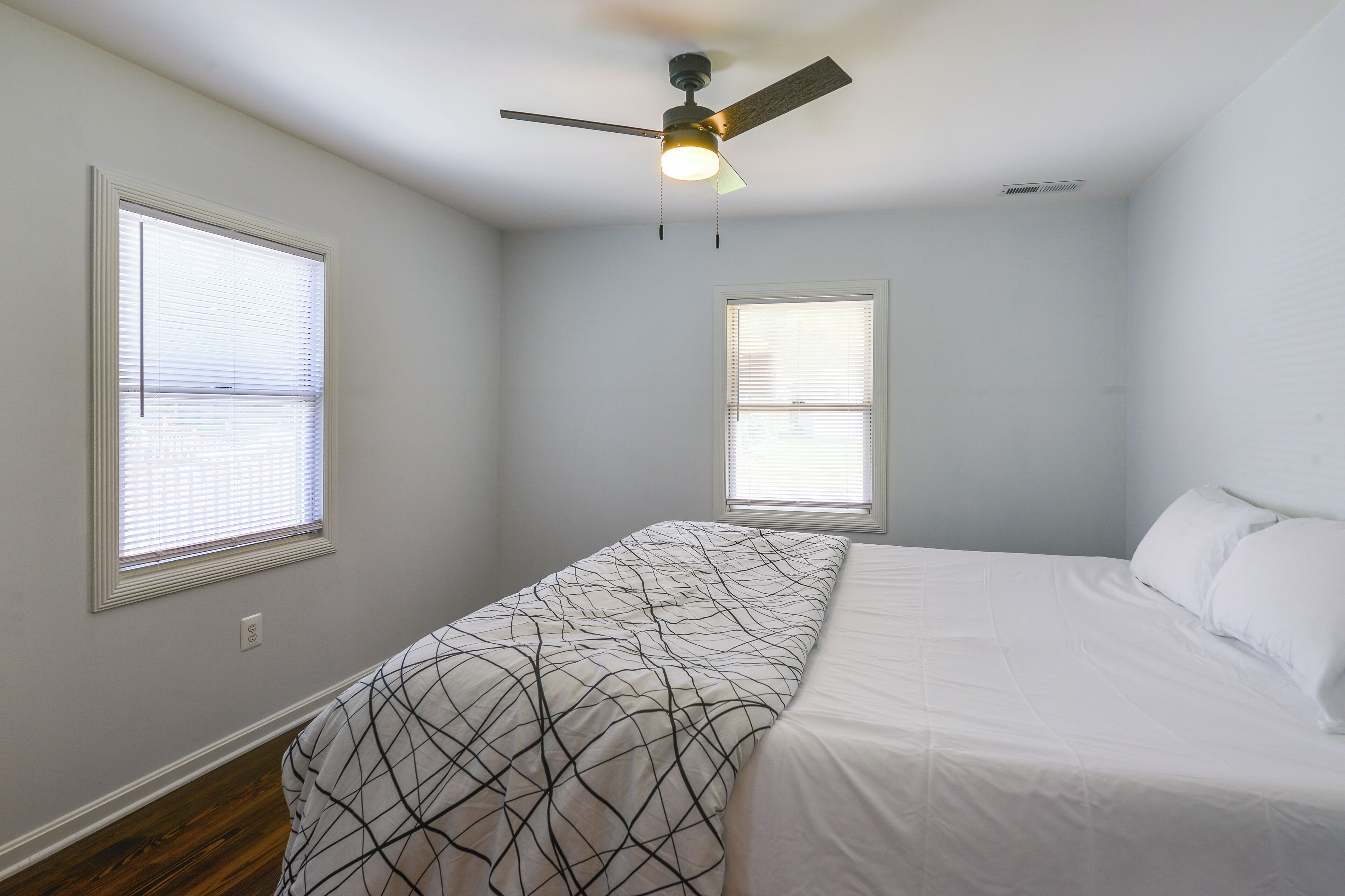 A bedroom with a bed, two windows, a ceiling fan, and a light fixture.