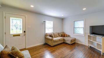 A living room with hardwood flooring, a sectional sofa, a television, and a window with blinds.