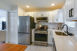 A modern kitchen with stainless steel appliances, white cabinetry, and a marble countertop.