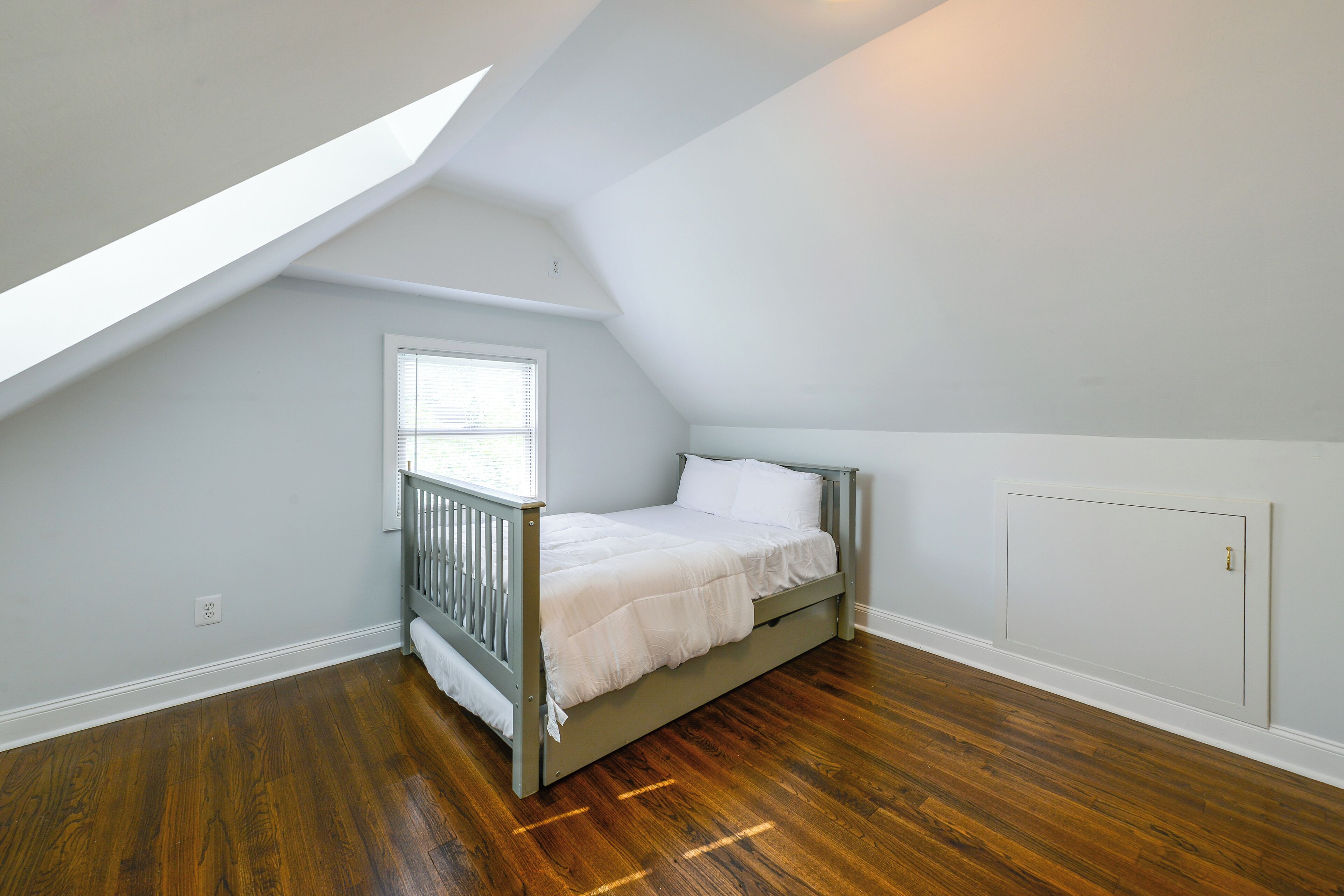 A bedroom with a sloped ceiling, a single bed, a window with blinds, and a radiator.