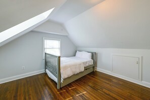 A bedroom with a sloped ceiling, a single bed, a window with blinds, and a radiator.