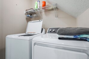 A laundry area with a front-loading washing machine and a dryer, a shelf with cleaning supplies, and a folded towel on the dryer.