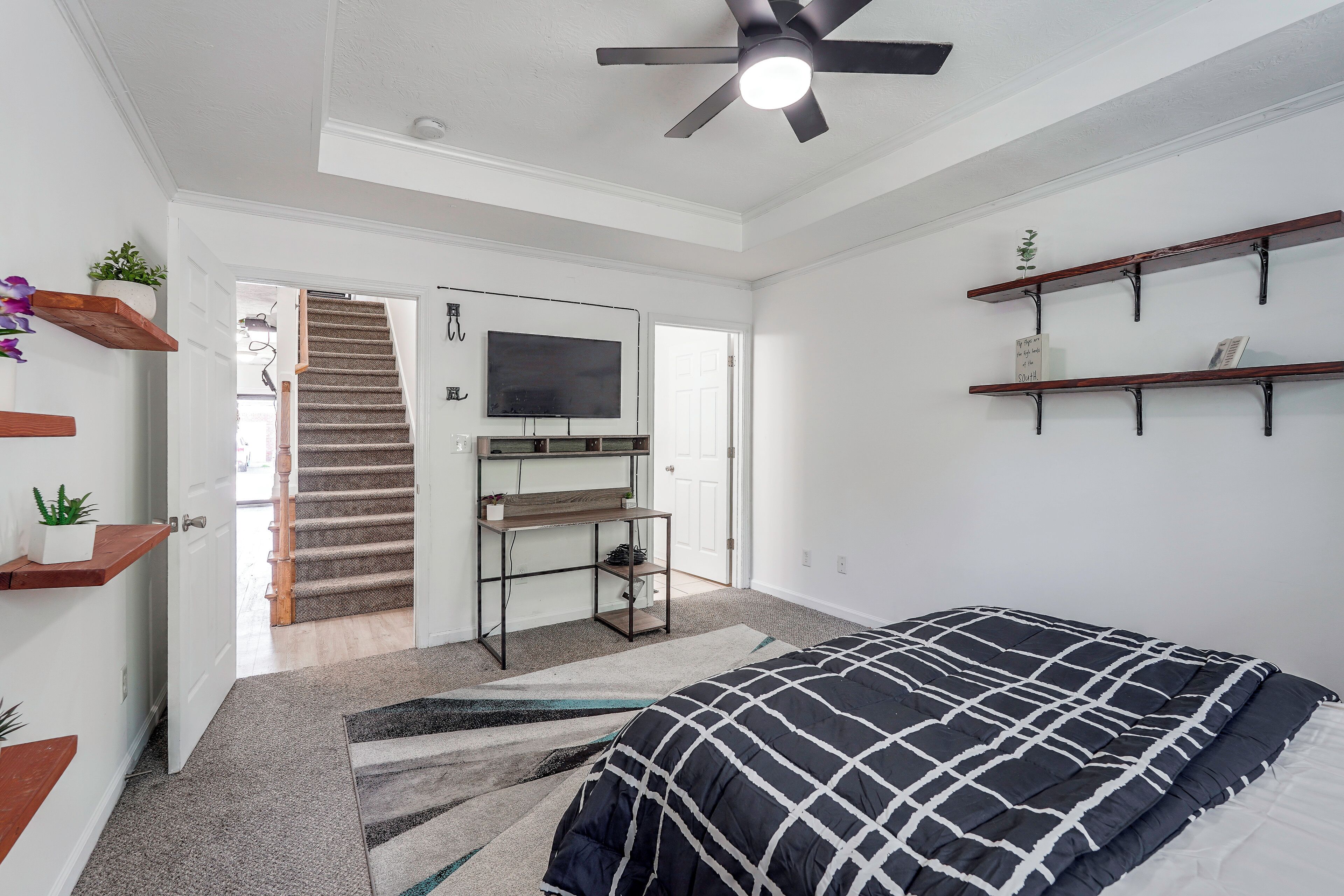 A bedroom with a bed, a TV, a desk, and a ceiling fan.