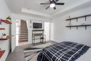 Un dormitorio con cama, televisor, escritorio y ventilador de techo.