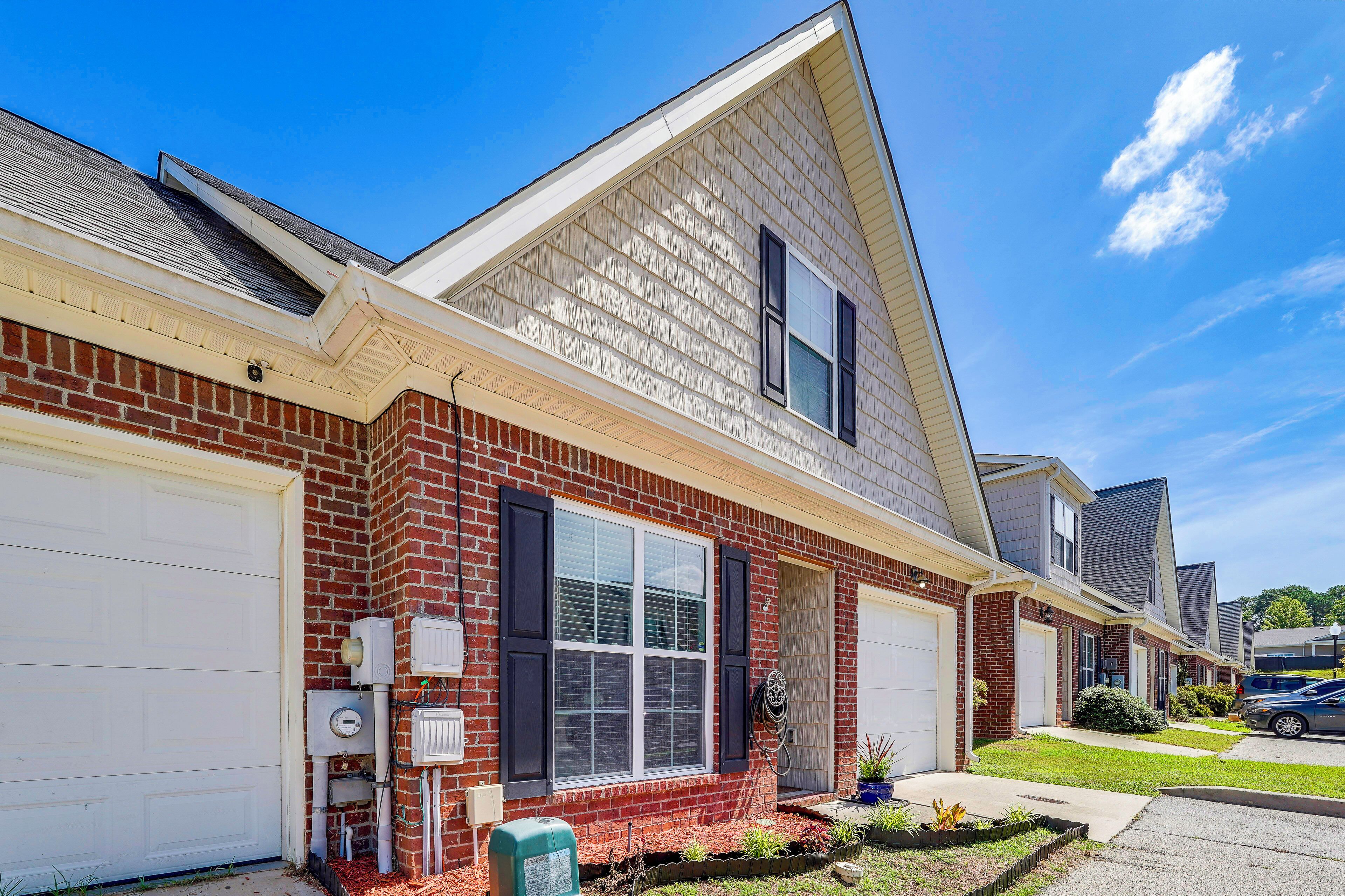 A two-story residential building with a brick facade, white garage doors, and a small front yard with landscaping.