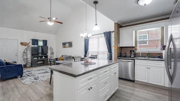 A modern kitchen with white cabinets, a stainless steel refrigerator, and a dining area with a blue sofa and a fireplace.
