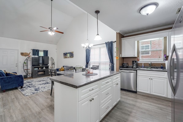 Una cocina moderna con armarios blancos, un refrigerador de acero inoxidable y un comedor con un sofá azul y una chimenea.