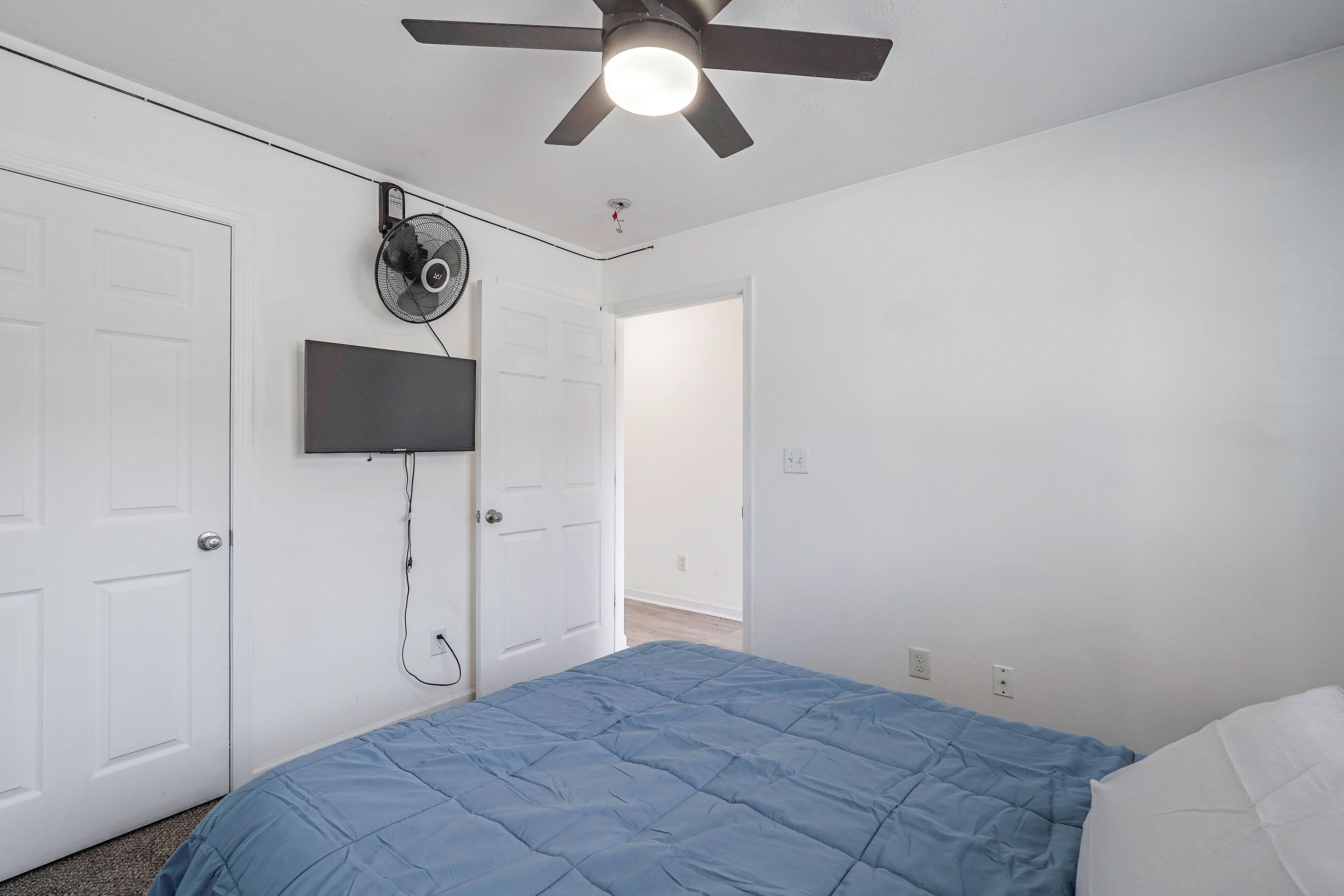 Ein Schlafzimmer mit Bett, Deckenventilator, einem angebrachten Fernseher und einer Tür.