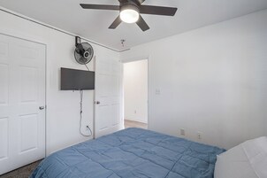 Un dormitorio con cama, ventilador de techo, televisor montado y una puerta.