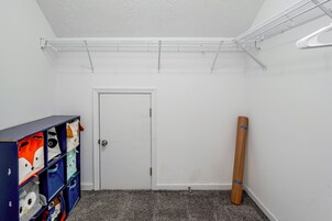 Una habitación con una puerta blanca, un mueble azul con objetos de colores, una alfombra gris y un techo blanco con un estante metálico.