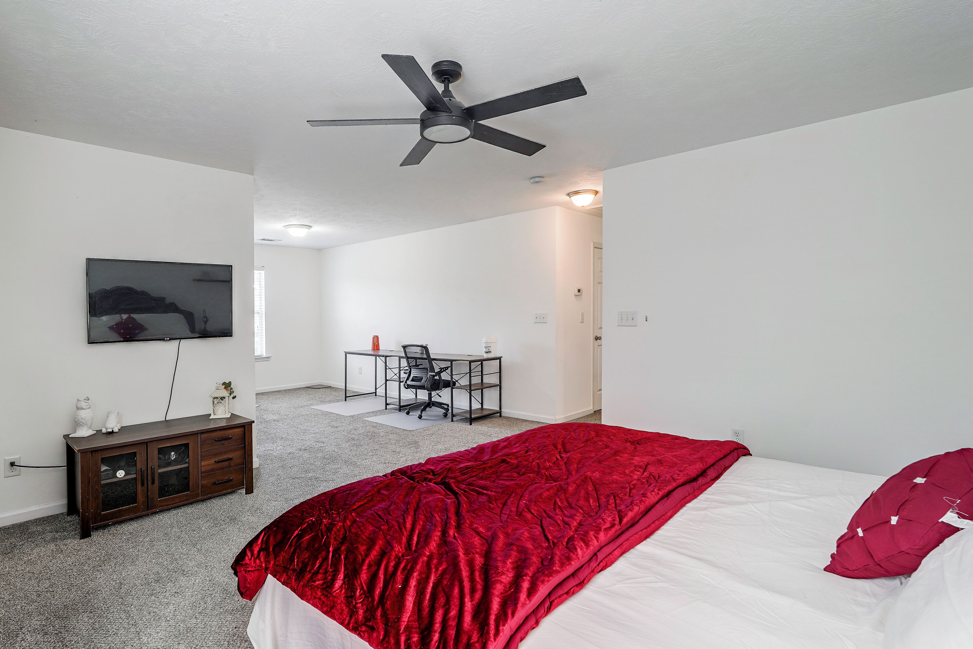 Un dormitorio con cama, escritorio, silla, televisión y ventilador de techo.