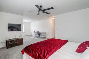 Un dormitorio con cama, escritorio, silla, televisión y ventilador de techo.