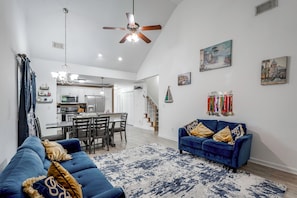 Uma sala de estar ampla com um sofá azul, uma área de refeições e uma cozinha ao fundo.
