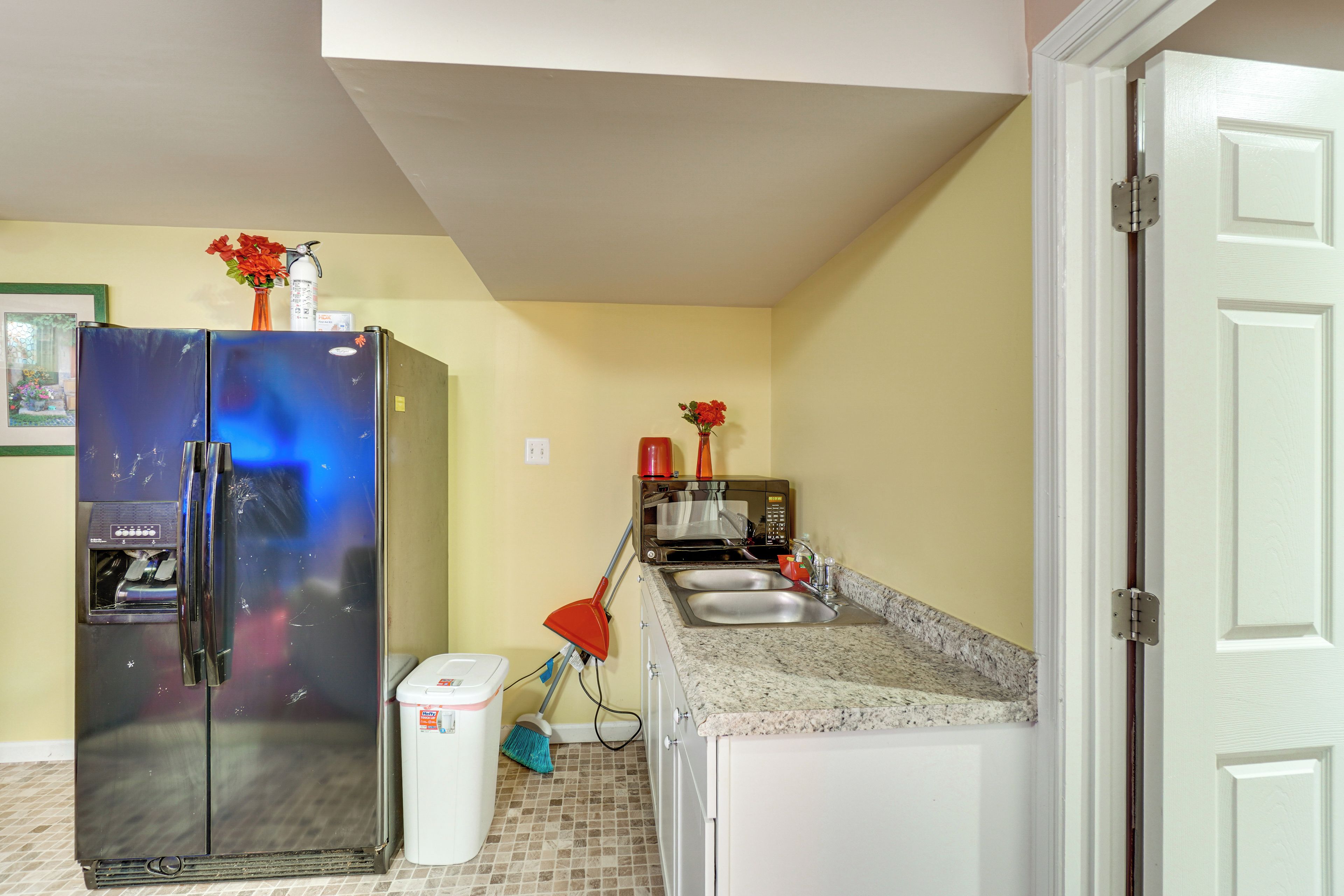Cocina compacta con refrigerador, microondas, pileta y escoba.