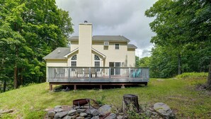 A two-story house with a balcony, surrounded by trees and a grassy area. - Poconos Getaway w/ Private Ski Slope & Pool Access (East Stroudsburg)