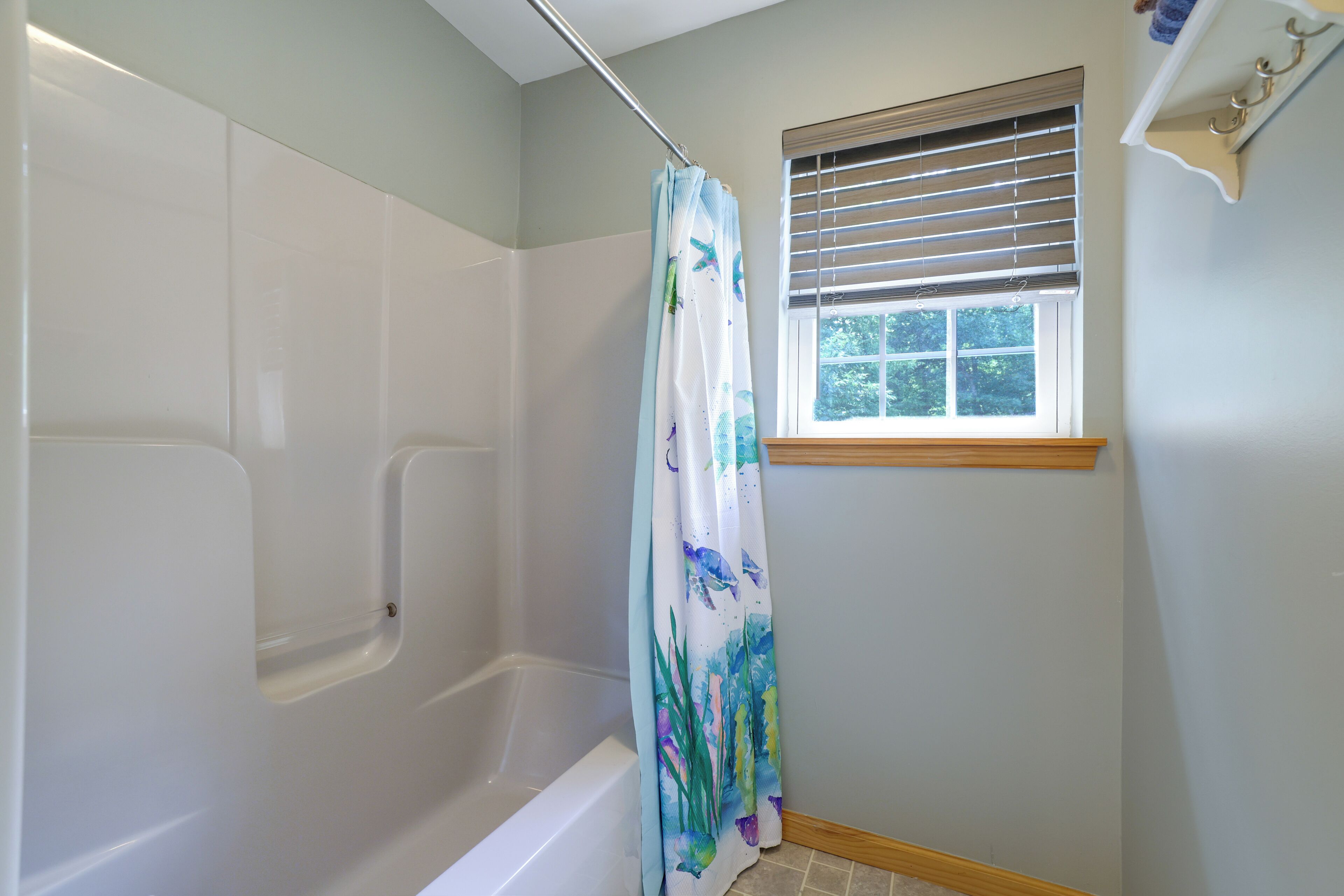 A bathroom with a shower, a window with blinds, and a towel rack.