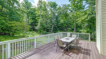 A wooden deck with a table and chairs, surrounded by a white railing, overlooking a forested area.