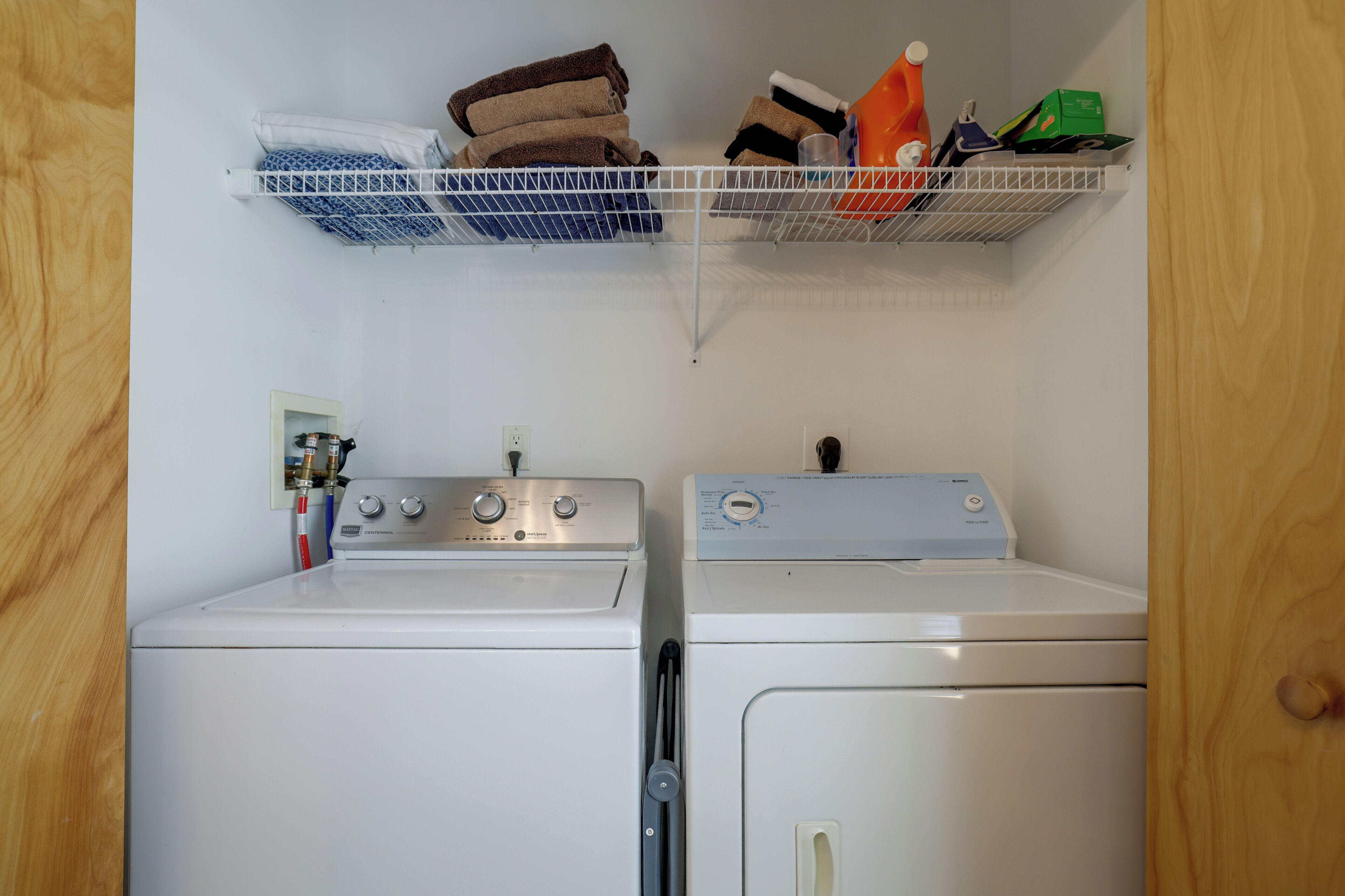 A laundry area with two washing machines, a shelf with folded towels, and a detergent bottle.