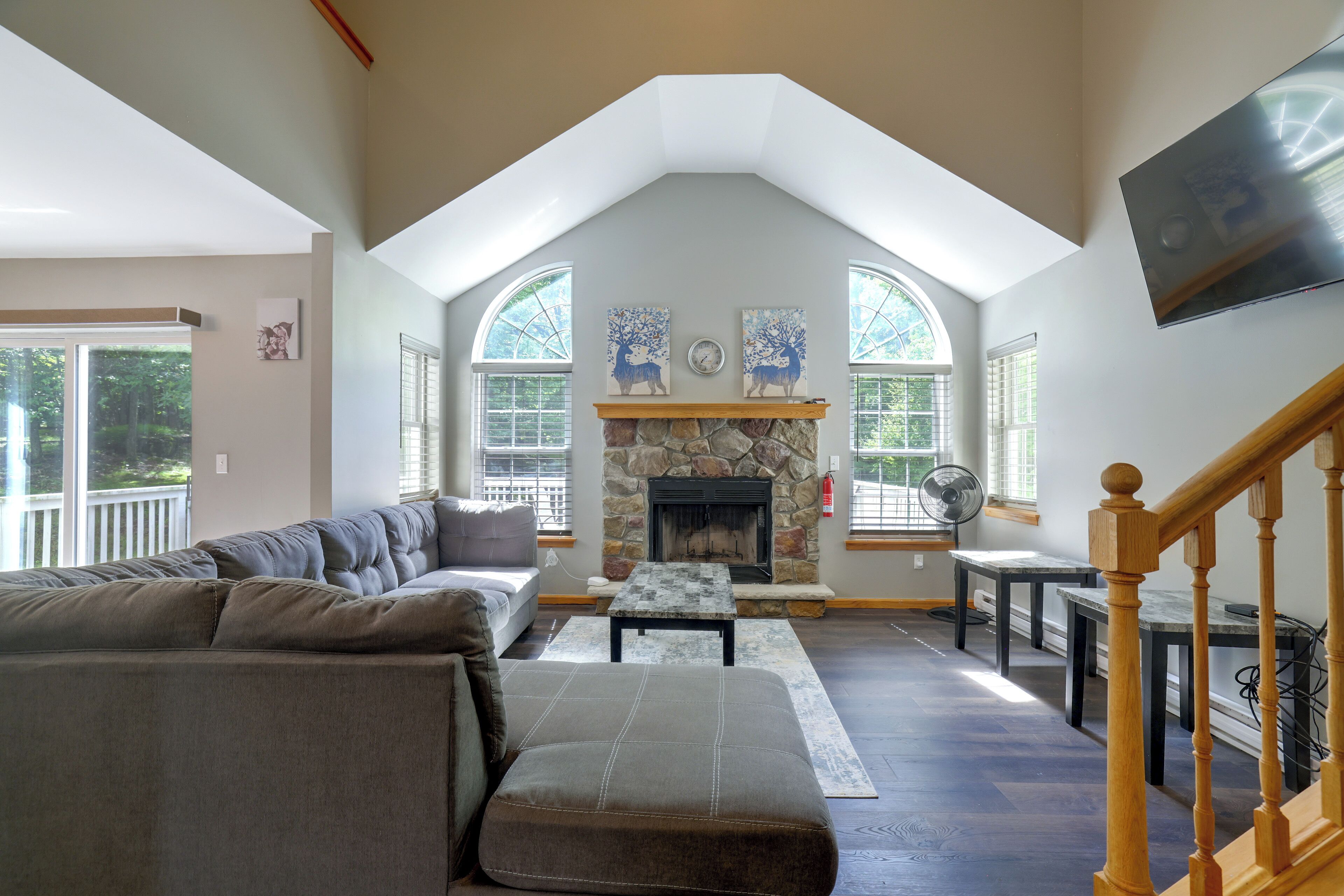 A spacious living room with a stone fireplace, a large sofa, and a television mounted on the wall.